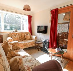 A sitting room with patterned sofas a small wooden table a wall mounted television and red curtains at The Lodge in Coltishall