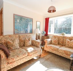 A sitting room with two patterned sofas a table lamp and a large window with red curtains at The Lodge in Coltishall