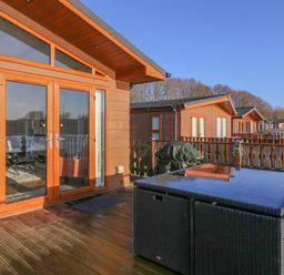 A wooden deck with a rattan table and glass door entrance at Shore Beats Work - Capenwray 10 in South Lakeland Leisure Village
