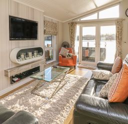 A living room with black leather sofas an orange armchair a glass coffee table and a wall-mounted TV at Shore Beats Work - Capenwray 10 South Lakeland Leisure Village