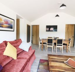 A living room with a red sofa and cushions a wooden dining table with chairs a wall-mounted tv and framed artwork at Whitehands Farm Barn in Old Buckenham