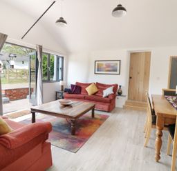 A living room with red sofas a wooden coffee table and a dining table with chairs at Whitehands Farm Barn in Old Buckenham