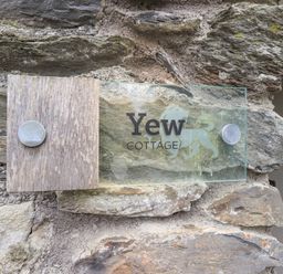 A glass and wood sign attached to a stone wall reading Yew Cottage at Backbarrow