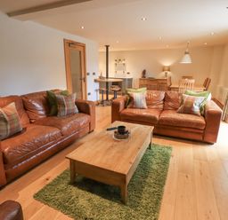A living room with two leather sofas and a wooden coffee table on a green rug at Yew Cottage in Backbarrow