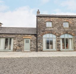 Stone exterior of a building with multiple green doors and windows with curtains at Lime Cottage in Backbarrow near Newby Bridge