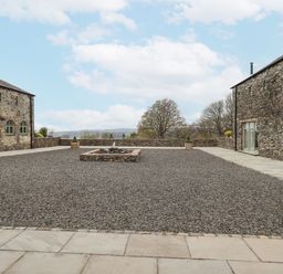 A gravel courtyard with a central stone water feature surrounded by stone buildings at Lime Cottage Backbarrow near Newby Bridge