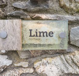 A stone wall with a glass and wood sign reading Lime Cottage at Lime Cottage in Backbarrow near Newby Bridge