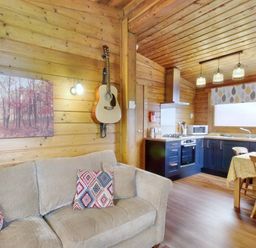 A wooden living room and kitchen with a sofa with patterned cushions a guitar on the wall and a dining table with chairs at Harbottle Lodge in Longframlington near Alnwick