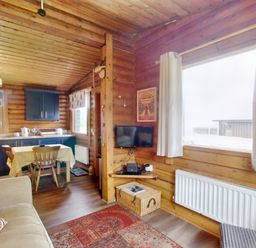 A wooden cabin interior with a kitchen area dining table and chairs a sofa and a window with curtains at Harbottle Lodge in Longframlington near Alnwick