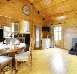 A wooden interior with a dining table set for four a kitchen area a wood burning stove and a TV at Acorn Lodge in Saxmundham