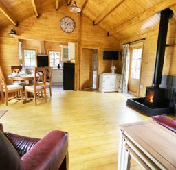 A wooden living room with a dining table and chairs a stove and a television at Acorn Lodge in Saxmundham