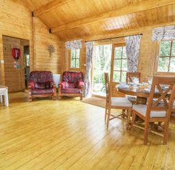 A wooden living room with three red leather armchairs a wooden dining table with four chairs and curtains on windows at Acorn Lodge in Saxmundham