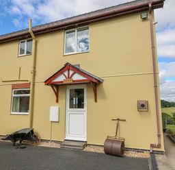The exterior of a beige house with a white door and windows and garden tools outside at Foxes Meadow in Howey near Llandrindod Wells