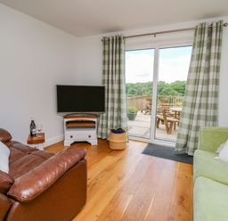 A living room with brown leather armchair green sofa TV and glass doors opening to a patio at Foxes Meadow in Howey near Llandrindod Wells