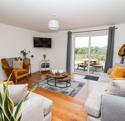 A living room with a gray sofa and armchair a wooden coffee table and sliding glass doors at Pheasant Wood in Howey near Llandrindod Wells