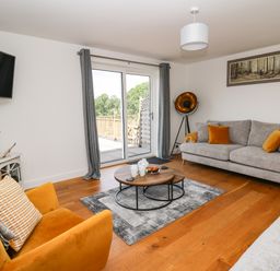 A living room with grey sofas and orange cushions a yellow armchair wooden floor and a coffee table at Pheasant Wood in Howey near Llandrindod Wells