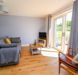 A living room with a gray sofa a wooden coffee table a small TV on a stand a leather armchair and sliding glass doors with gray curtains at Owl Cottage in Llandrindod Wells