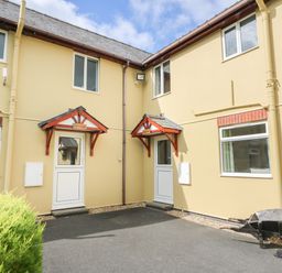 The exterior of a beige building with two white doors under wooden canopies and several windows with a paved area and a wheelbarrow near the wall at Owl Cottage in Llandrindod Wells