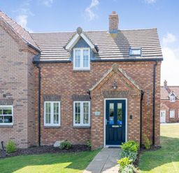 Front view of a brick house with white framed windows and blue door with pathway and grass at Lilipad Cottage The Bay near Filey
