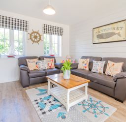 A living room with two brown leather sofas, a wooden coffee table, nautical cushions, wall decoration of a whale and ship wheel, at Lilipad Cottage in The Bay near Filey
