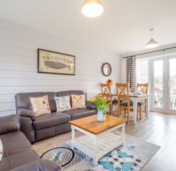 A living room with two brown sofas a wooden coffee table dining table with four chairs and glass doors at Lilipad Cottage The Bay near Filey