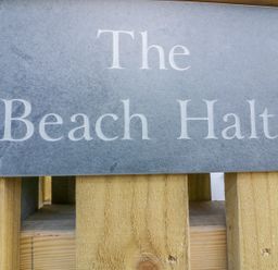 A close-up of a stone plaque with the text The Beach Halt mounted on a wooden fence