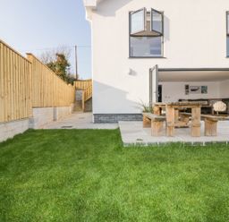 A backyard with green grass wooden fence and patio with wooden table and benches at The Beach Halt in Perranporth