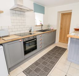 A kitchen with gray cabinets wooden countertops a stove sink microwave toaster and a rug on the tiled floor at Bryn Alun in Tanygrisiau near Blaenau Ffestiniog