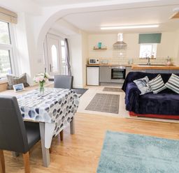 A kitchen and dining area with a small table and two chairs a sofa with cushions and a kitchen unit with oven fridge and microwave at Bryn Alun in Tanygrisiau near Blaenau Ffestiniog