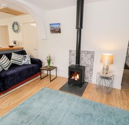 A living room with a blue sofa, wood burning stove, side tables with flowers and a lamp at Bryn Alun in Tanygrisiau near Blaenau Ffestiniog