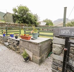 An outdoor stone patio area with flower pots on a stone ledge and a green wooden fence at Bryn Alun in Tanygrisiau near Blaenau Ffestiniog