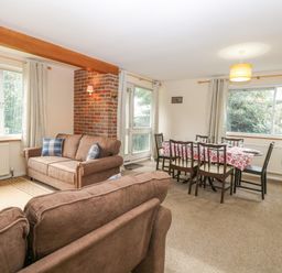 A living room with brown sofas and a dining table with six chairs and a floral tablecloth at Swan Dyke Cottage Horning near Wroxham