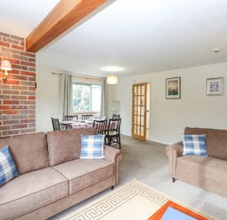 A living room with two brown sofas and plaid cushions and a dining table with chairs near a window at Swan Dyke Cottage in Horning near Wroxham