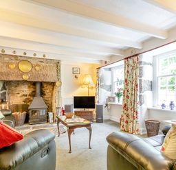 A living room with leather chairs a stone fireplace with a stove floral curtains and a television at Westside Cottage in Cardinham near Bodmin