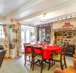 A dining room with a red tablecloth on the table and a large stone fireplace at Westside Cottage in Cardinham near Bodmin