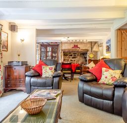 A living room with leather armchairs and a read table near a stone fireplace at Westside Cottage in Cardinham near Bodmin