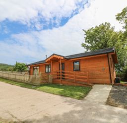 A wooden cabin with a ramp and fenced yard under a partly cloudy sky at Chale Farm Lodge in Chale