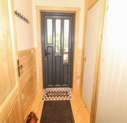 A hallway with a black door at the end a welcome mat a coat hook on the wall and wooden paneling at Chale Farm Lodge in Chale