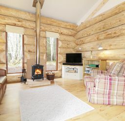 A living room with a wood stove between two tall windows a leather sofa a plaid armchair a TV on a cabinet and a bookshelf at Heron Lodge in North Kessock