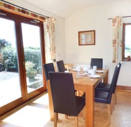A dining room with a wooden table set with white crockery and six black chairs at The Old Granary in Spittal