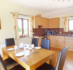 A kitchen and dining area with a wooden table set with cups and plates and black chairs at The Old Granary in Spittal