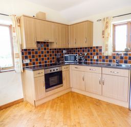 A kitchen with wooden cabinets tiled backsplash and wooden floor at The Old Granary in Spittal