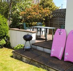 A garden patio with a table and chairs a small barbecue and two pink bodyboards at Pendeen in Wadebridge