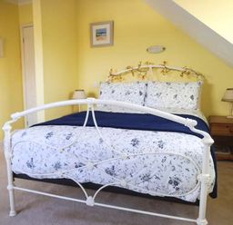 A bedroom with a white metal bed frame decorated with string lights a wooden nightstand with a lamp and yellow walls at Pendeen in Wadebridge