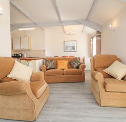 A living room with two armchairs and a sofa with cushions next to a kitchen area at The Cottage Chilsworthy near Holsworthy