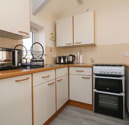 A kitchen with white cabinets a microwave dish rack kettle toaster and stove at The Cottage in Chilsworthy near Holsworthy