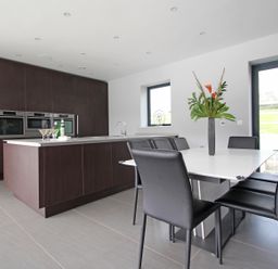 A kitchen with dark cabinets island with drinks white dining table with black chairs and a vase with flowers at Ancarva near Kingsands