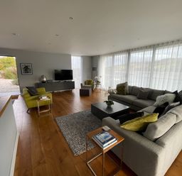 A living room with sofas a cabinet television and large windows with sheer curtains at Ancarva Near Kingsands