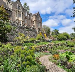 A garden with a curved brick pathway and stone terraces in front of a large stone house at Haslington House in Malvern