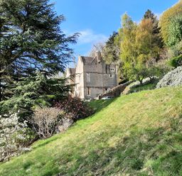 A stone house on a hillside surrounded by trees and shrubs at Haslington House in Malvern